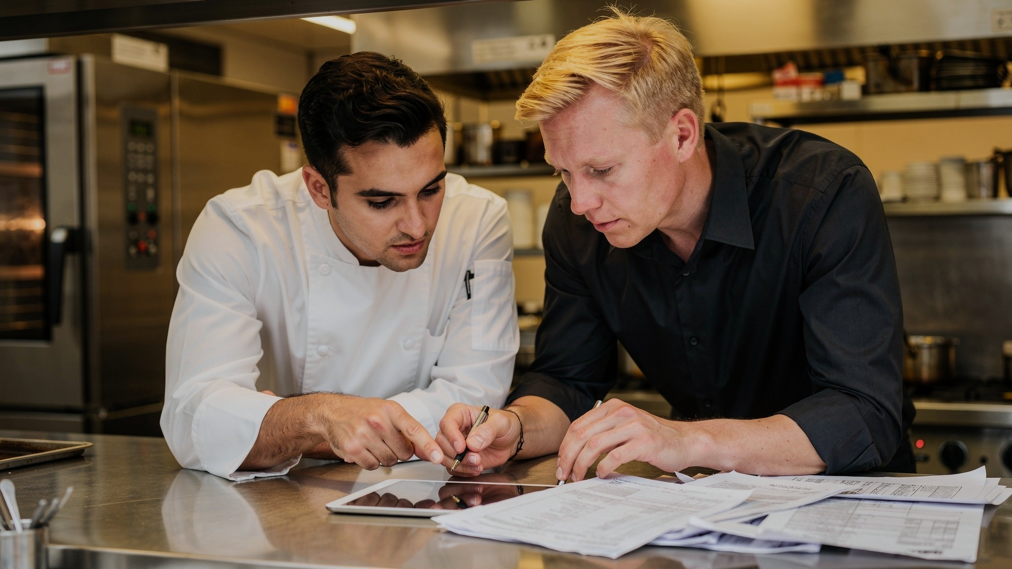 Restaurant chef and manager reviewing inventory variance reports and tablet data together at kitchen counter
